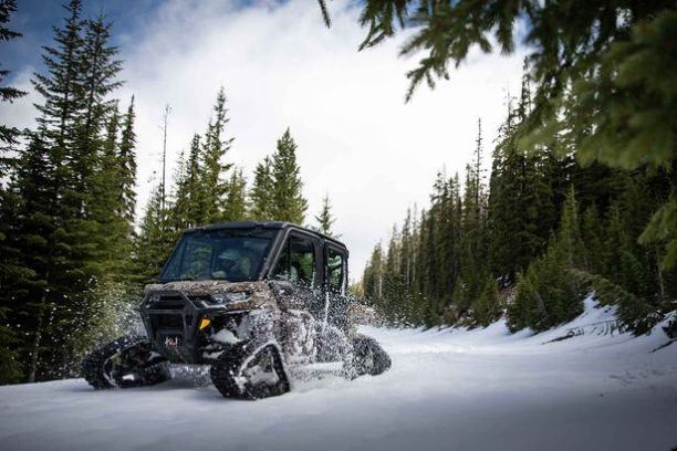 Off-road vehicle with tracks driving through snowy forest path.