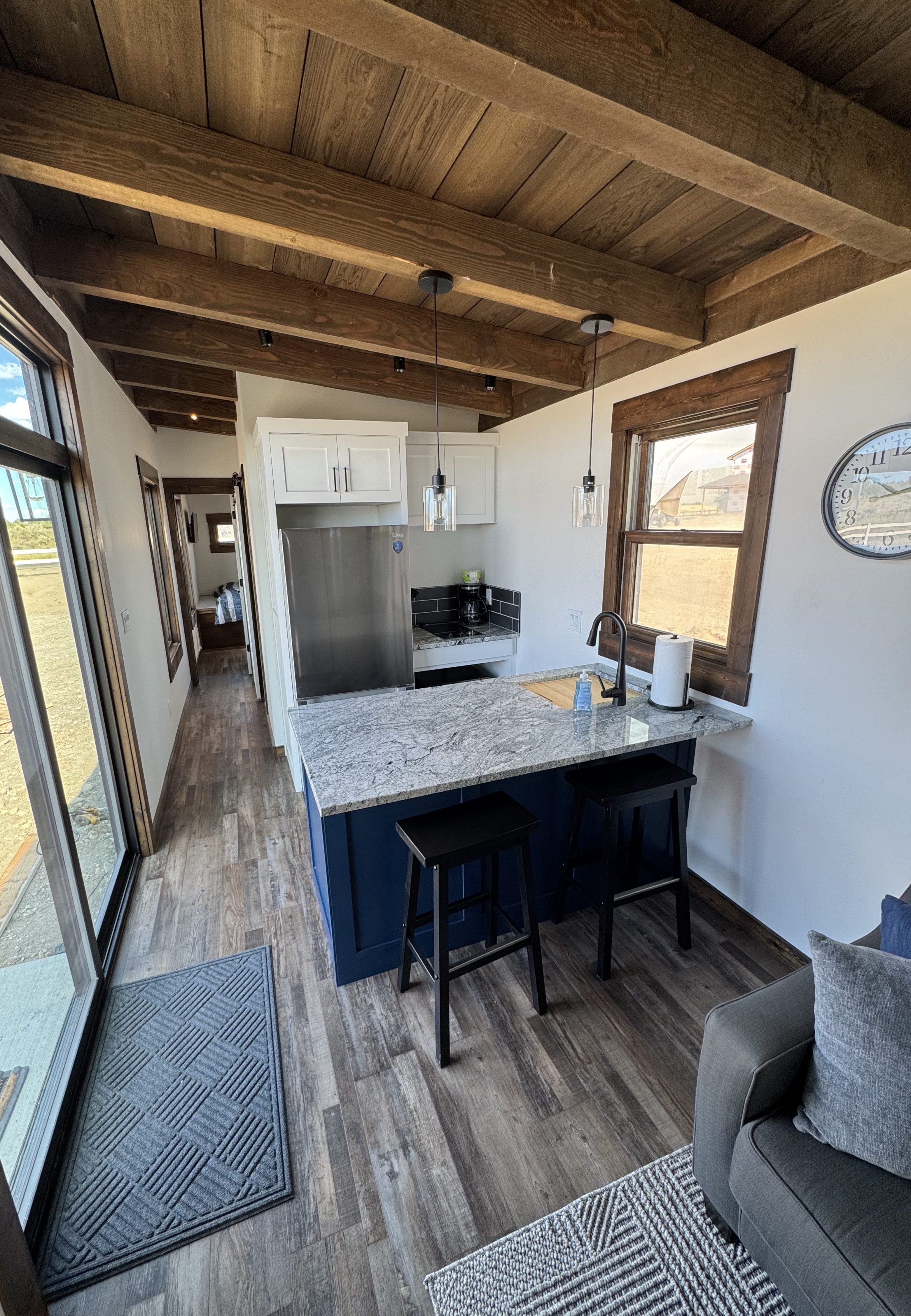 Modern kitchen with wood beams, island, gray countertops, and a large window.